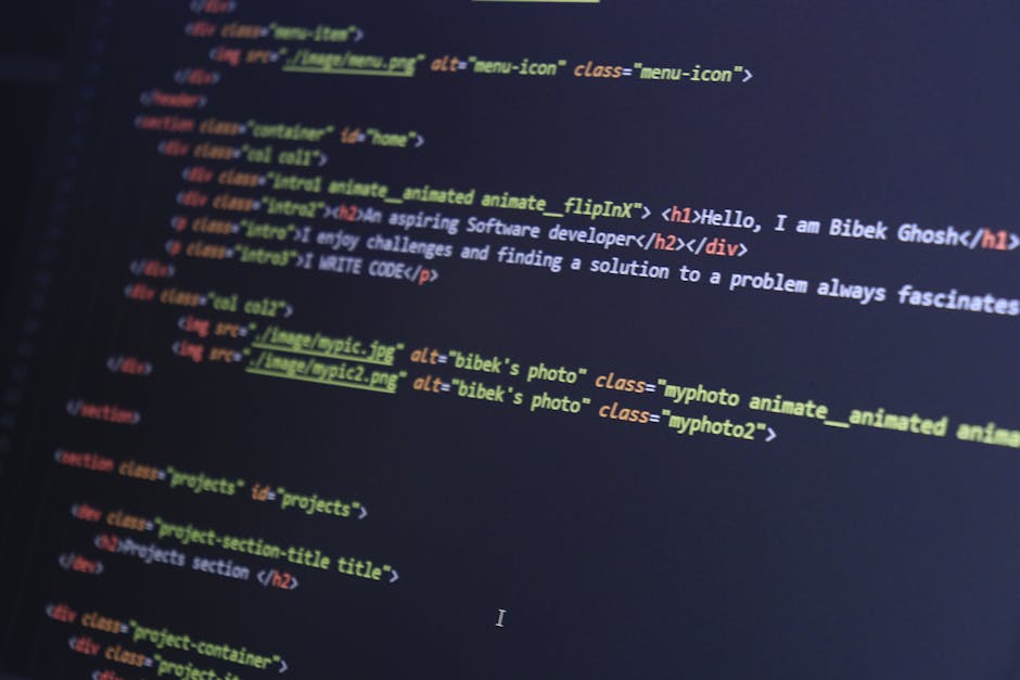 A close-up of a person's right hand typing on a silver laptop keyboard situated on a wooden surface, with the screen displaying lines of programming code in a dark background. The person is wearing a 